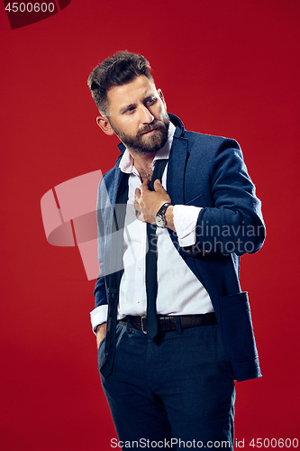 Image of Male beauty concept. Portrait of a fashionable young man with stylish haircut wearing trendy suit posing over red background.