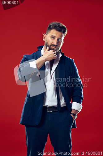 Image of Male beauty concept. Portrait of a fashionable young man with stylish haircut wearing trendy suit posing over red background.