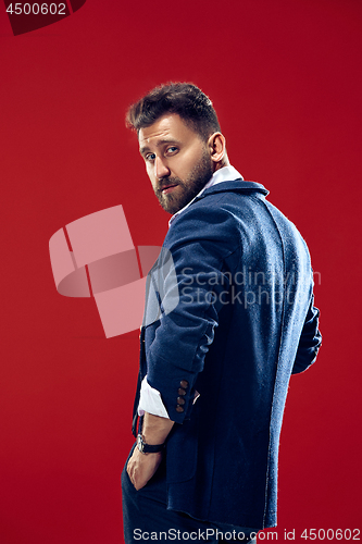 Image of Male beauty concept. Portrait of a fashionable young man with stylish haircut wearing trendy suit posing over red background.