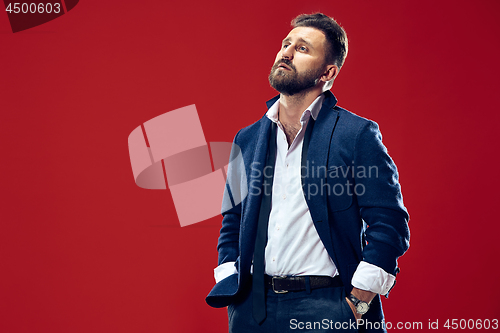 Image of Male beauty concept. Portrait of a fashionable young man with stylish haircut wearing trendy suit posing over red background.