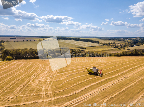 Image of Countryside landscape aerial view from drone to agricultural field with combine on a blue sky background.