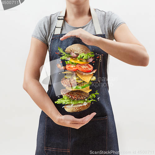 Image of Big homemade fresh burger in the girl\'s hands from flying ingredients - fresh vegetables and organic natural beef meat on a white background.