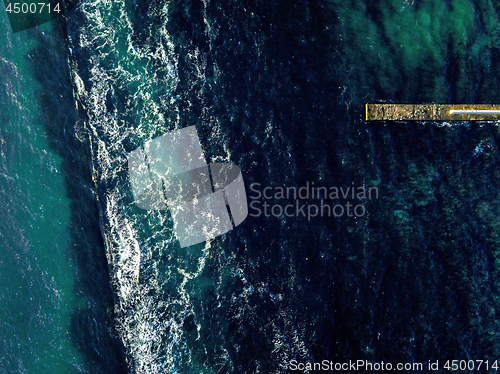 Image of Aerial view from drone to a seascape of turquoise color water and stone mole in a sea clear water with foam waves. Top view. Copy space.