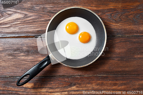 Image of Fried eggs in a frying pan on a wooden background with copy space. Breakfast from natural fresh products. Top view.