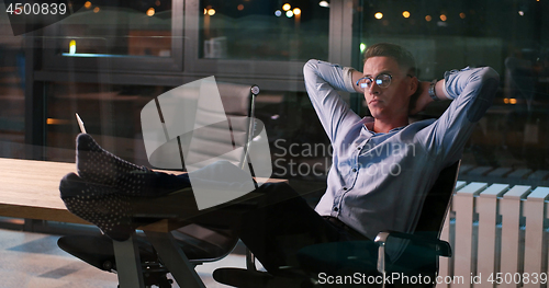 Image of businessman sitting with legs on desk at office