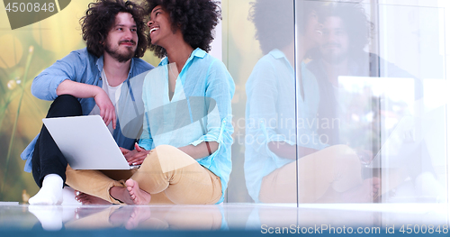 Image of multiethnic couple using a laptop on the floor