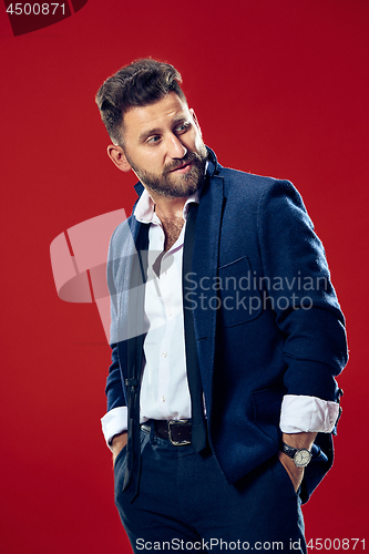 Image of Male beauty concept. Portrait of a fashionable young man with stylish haircut wearing trendy suit posing over red background.