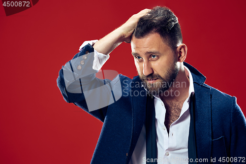 Image of Male beauty concept. Portrait of a fashionable young man with stylish haircut wearing trendy suit posing over red background.