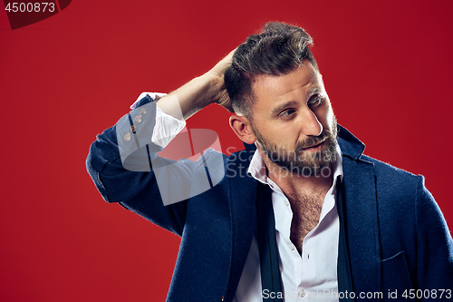 Image of Male beauty concept. Portrait of a fashionable young man with stylish haircut wearing trendy suit posing over red background.