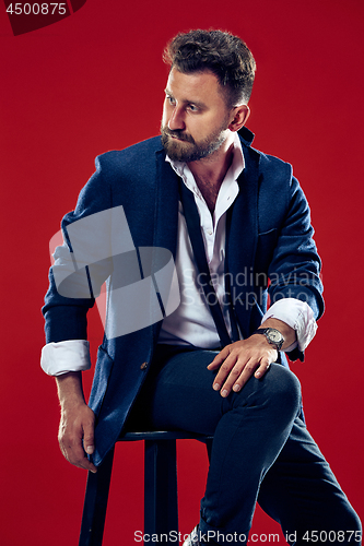 Image of Male beauty concept. Portrait of a fashionable young man with stylish haircut wearing trendy suit posing over red background.