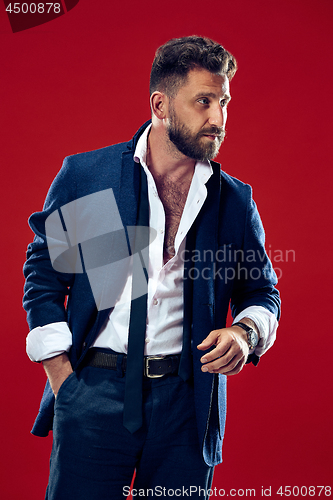 Image of Male beauty concept. Portrait of a fashionable young man with stylish haircut wearing trendy suit posing over red background.