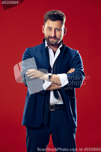 Image of Male beauty concept. Portrait of a fashionable young man with stylish haircut wearing trendy suit posing over red background.