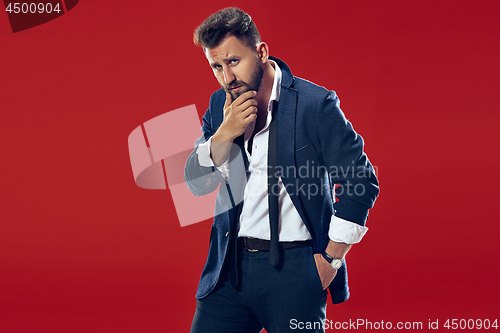 Image of Suspiciont. Doubtful pensive man with thoughtful expression making choice against red background