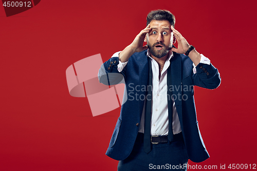 Image of The young attractive man looking suprised isolated on red