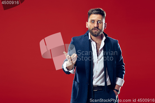 Image of The young attractive man looking suprised isolated on red