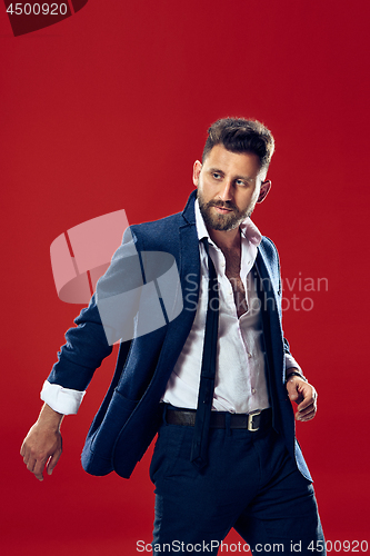 Image of Male beauty concept. Portrait of a fashionable young man with stylish haircut wearing trendy suit posing over red background.