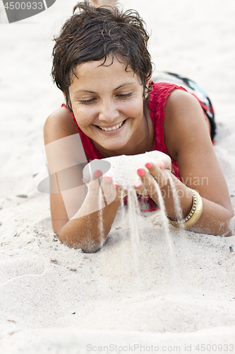 Image of Attractive brunet woman in red lying on a sand.