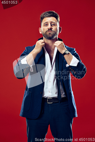 Image of Male beauty concept. Portrait of a fashionable young man with stylish haircut wearing trendy suit posing over red background.