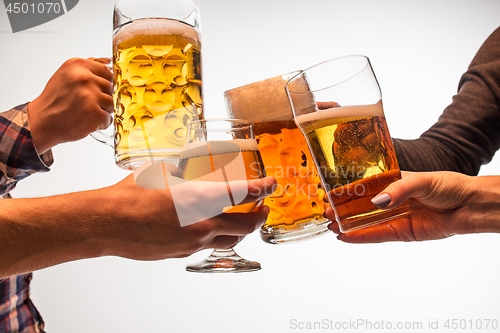 Image of hands with mugs of beer toasting creating splash isolated on white background