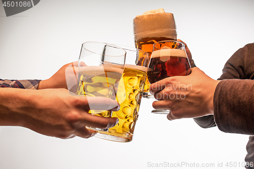 Image of hands with mugs of beer toasting creating splash isolated on white background