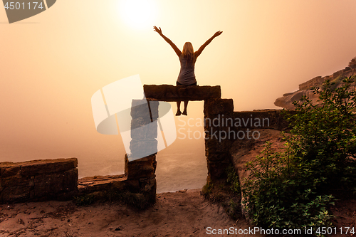 Image of Female sitting on ancient sandstone doorway with foggy sunrise