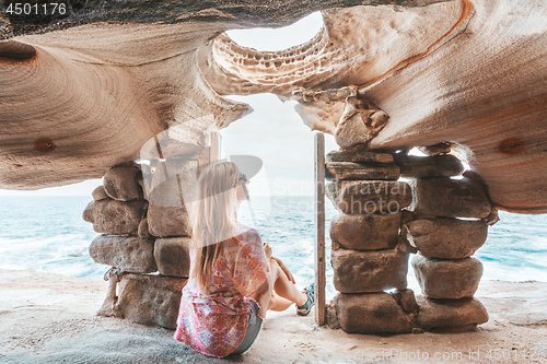 Image of Female sits inside cliff top cave watching the ocean