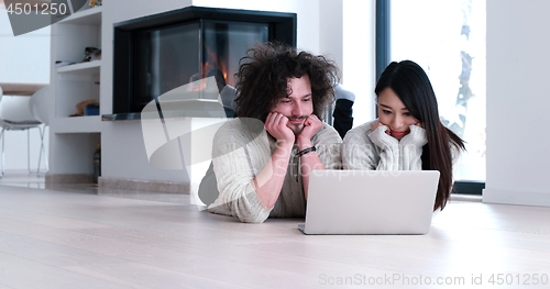 Image of young multiethnic couple using a laptop on the floor