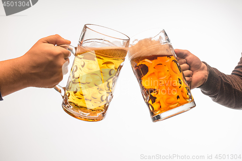 Image of hands with mugs of beer toasting creating splash isolated on white background