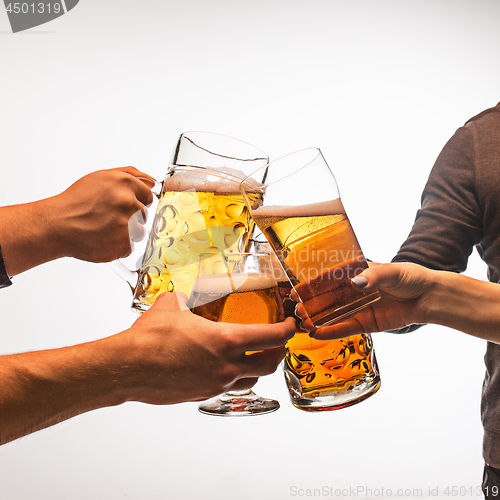 Image of hands with mugs of beer toasting creating splash isolated on white background