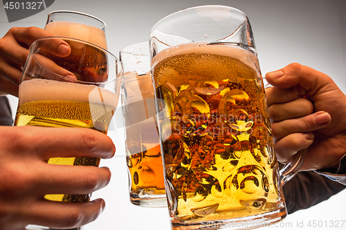 Image of hands with mugs of beer toasting creating splash isolated on white background