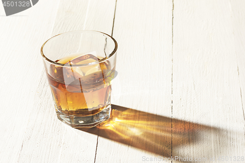 Image of Whiskey in glass, ice cub served in a short glass on white table