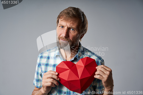 Image of Unhappy mature man in checkered shirt holding heart shape