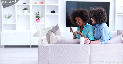 Image of multiethnic couple sitting on sofa at home drinking coffe