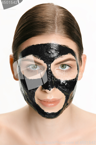 Image of Young beautiful woman applying a mask for the face of the therapeutic black mud. Spa treatment