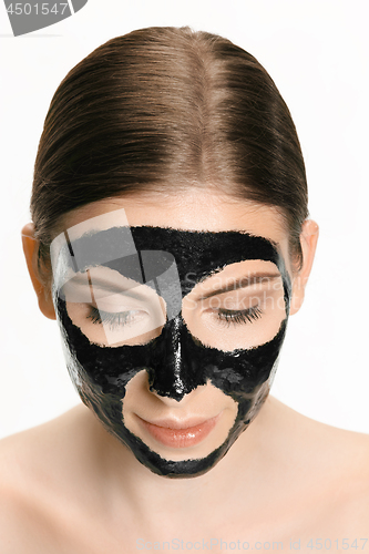 Image of Young beautiful woman applying a mask for the face of the therapeutic black mud. Spa treatment