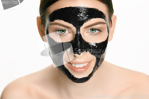 Image of Young beautiful woman applying a mask for the face of the therapeutic black mud. Spa treatment