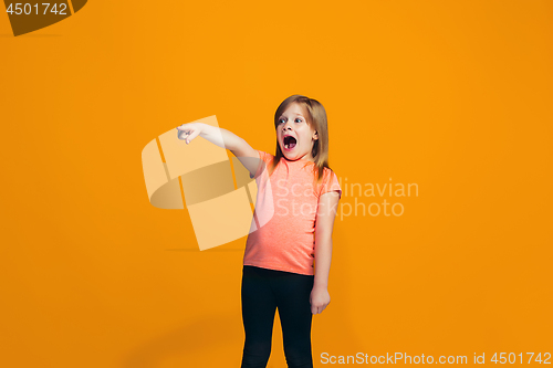 Image of The happy teen girl pointing to you, half length closeup portrait on orange background.