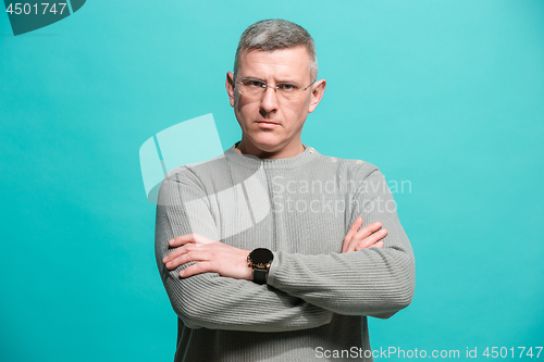 Image of The serious businessman standing and looking at camera against blue background.