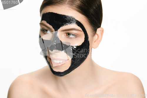 Image of Young beautiful woman applying a mask for the face of the therapeutic black mud. Spa treatment