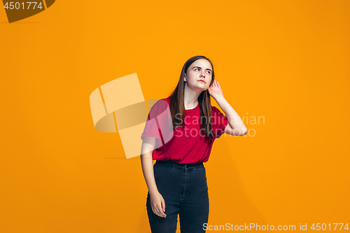 Image of The young teen girl whispering a secret behind her hand over orange background