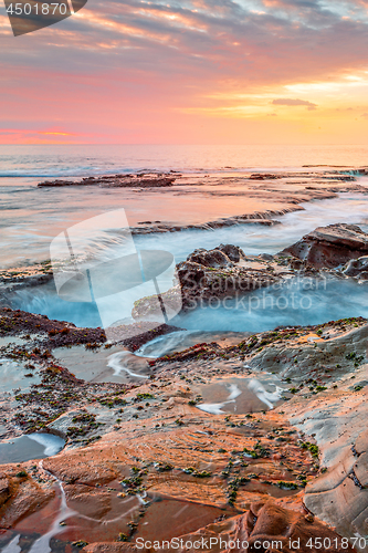 Image of Ocean flowing into coastal channels eroded into rock and a stunning sunrise