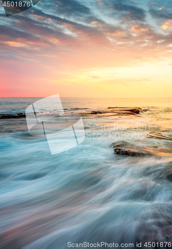 Image of Incoming waves wash over rocks at sunrise