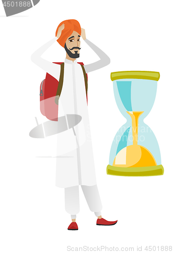 Image of Worried hindu traveler man looking at hourglass.