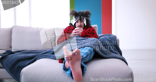 Image of sick man is holding a cup while sitting on couch