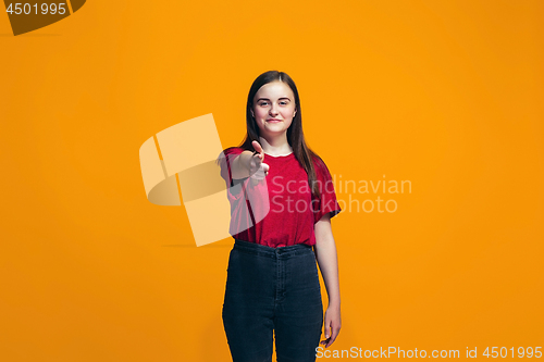 Image of The happy teen girl pointing to you, half length closeup portrait on orange background.