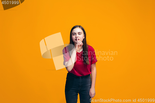 Image of The young teen girl whispering a secret behind her hand over orange background