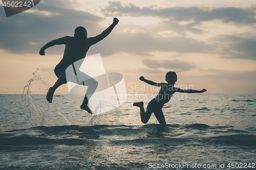 Image of Father and son playing on the beach at the sunset time.