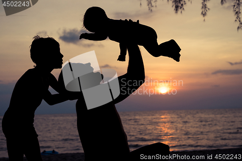 Image of Father and two sons  playing on the beach at the sunset time.