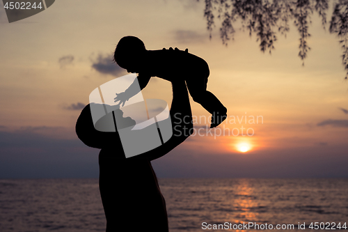 Image of Father and baby son  playing on the beach at the sunset time.