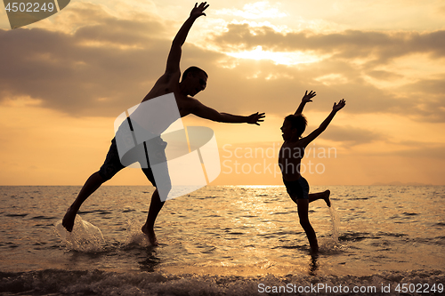 Image of Father and son playing on the beach at the sunset time.